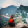 View of girl sitting on the edge of the rock with raised hands and taking pleasure of breathtaking forested mountains landscape of Machu Picchu